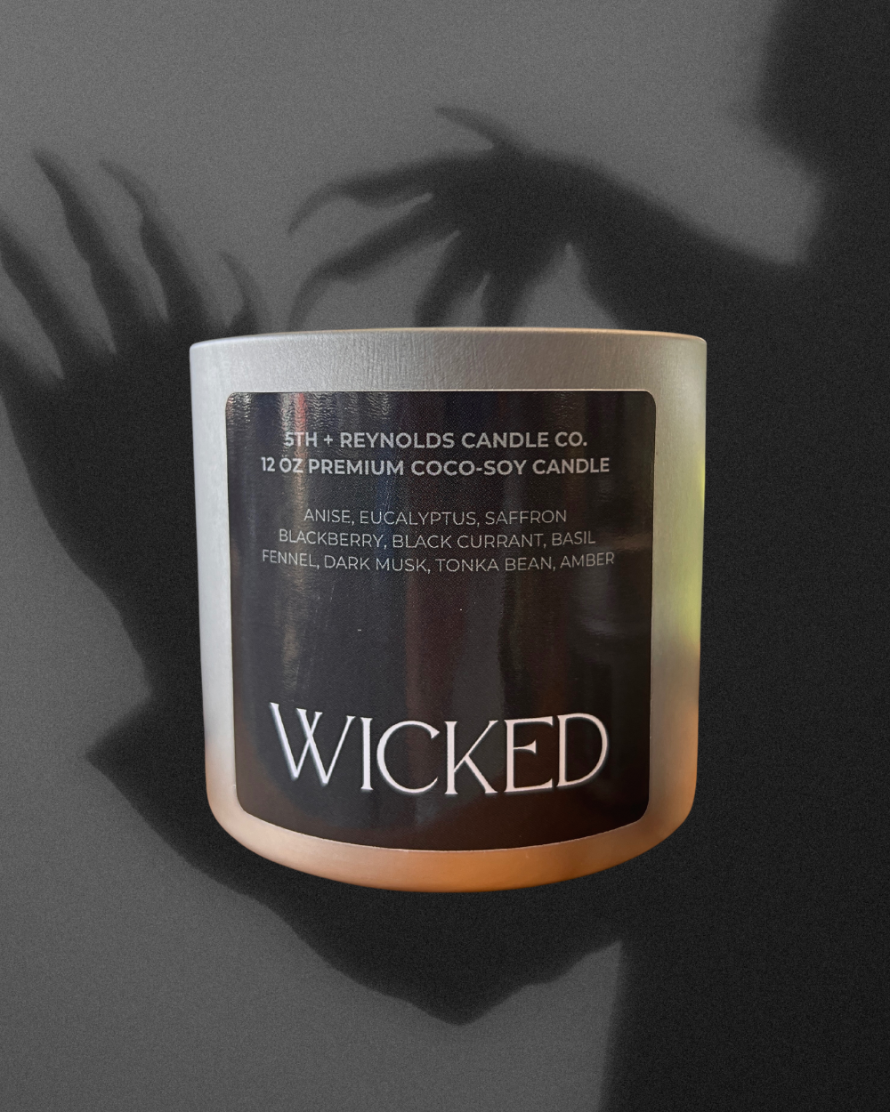 Candle labeled 'Wicked' by 5th + Reynolds Candle Co. on a dark background, showing shadows of a figure with creepy hands with claws.